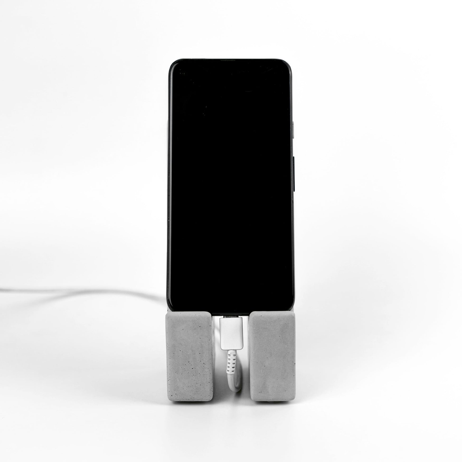 Design Handyhalter aus Beton mit Smartphone und Ladekabel auf weißem Hintergrund. Vorderansicht